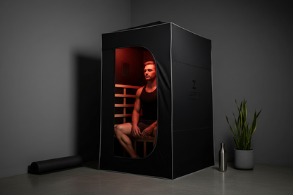 Person seated inside a sleek black portable infrared sauna in a minimalist home gym with warm infrared glow, performance-focused aesthetic